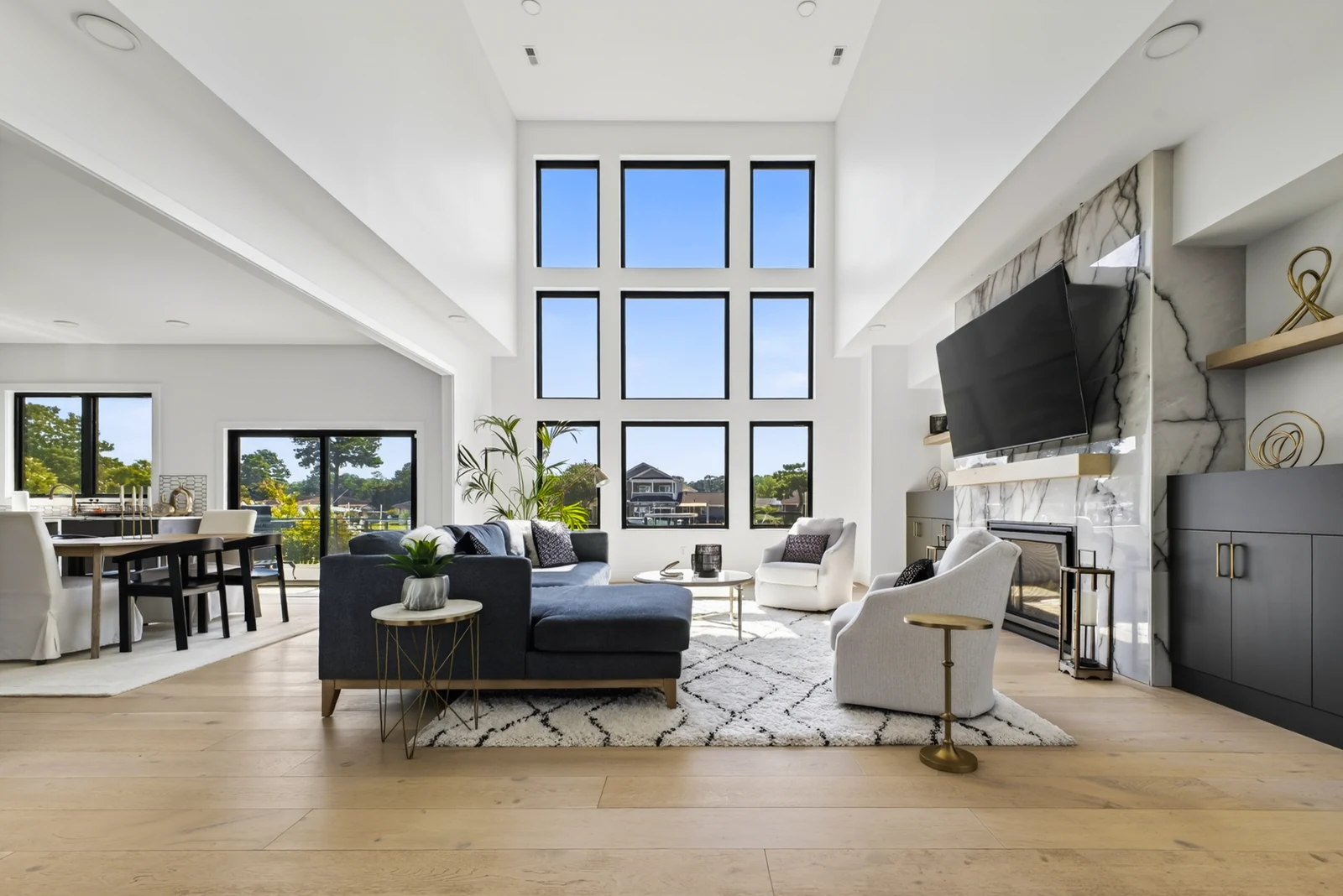 Sunlit living room with tall black-framed windows, a navy sectional and a marble fireplace